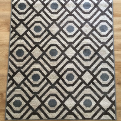 Tapete geométrico cinzento, preto e bege sobre chão de madeira clara