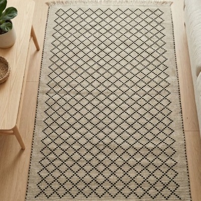 Tapete bege geometricamente padrão losangos pretos com franjas em ambiente de sala com chão de madeira