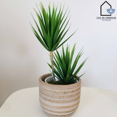 Planta artificial em vaso cerâmico bege com riscas brancas sobre superfície branca