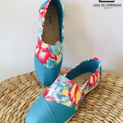 Sapatos alpercatas azuis com padrão floral colorido sobre superfície de palha