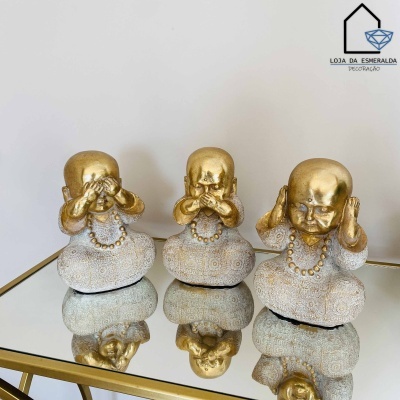 Três estatuetas decorativas de bebés dourados e brancos em mesa espelhada