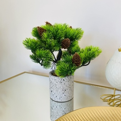 Mini planta artificial em vaso cinza sobre superfície espelhada com decoração dourada.