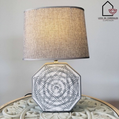 Candeeiro de mesa branco com padrão circular cinzento e cúpula bege em tecido numa mesa redonda com relevo floral.