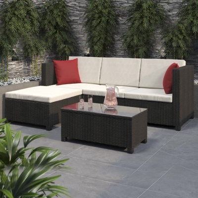 Conjunto sofá em vime sintético castanho com almofadas bege e vermelhas, mesa de centro, plantas ao fundo.