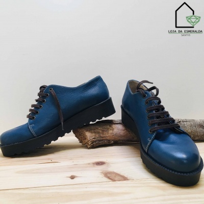 Sapatos azuis de couro com solas pretas e cadarços em fundo branco e madeira