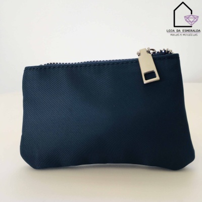 Carteira pequena azul escuro com fecho prateado sobre superfície branca, logo da loja ao fundo