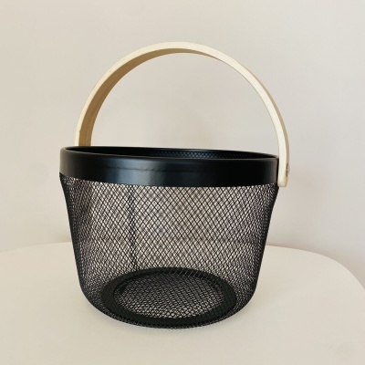Cesto preto de metal em rede com pega de madeira clara num fundo branco