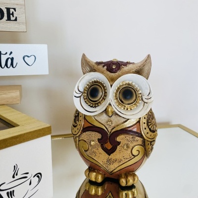 Estátua decorativa de coruja dourada e bronze com olhos grandes sobre superfície espelhada