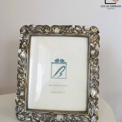 Moldura decorativa com padrão de folhas em metal prateado envelhecido, com logotipo e texto Balcosta Home 20CM X 25 CM.