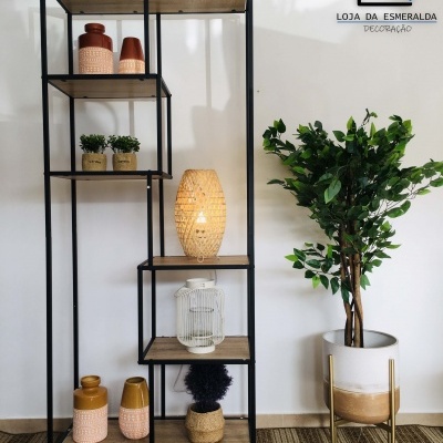 Estante metálica com prateleiras de madeira e decoração, planta artificial ao lado, parede branca com logo