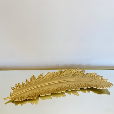 Prato dourado em forma de pena sobre superfície espelhada e fundo branco.