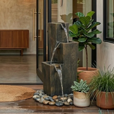 Fonte decorativa com três níveis, pedras e plantas junto a porta de vidro com puxadores dourados