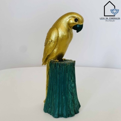 Estátua decorativa de papagaio dourado em tronco verde sobre superfície branca
