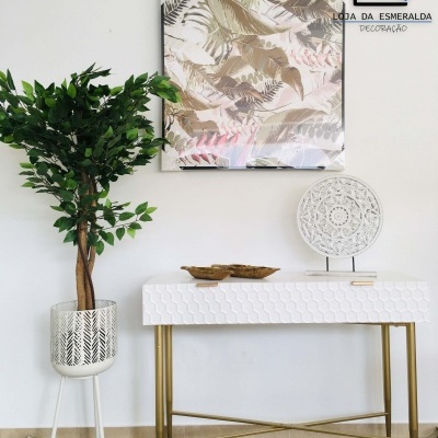 mesa consola branca com padrão hexagonal e pernas douradas, planta artificial em vaso branco, quadro com padrão de folhas e objeto decorativo redondo branco