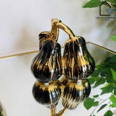 Escultura dourada e preta de três pêras sobre superfície espelhada