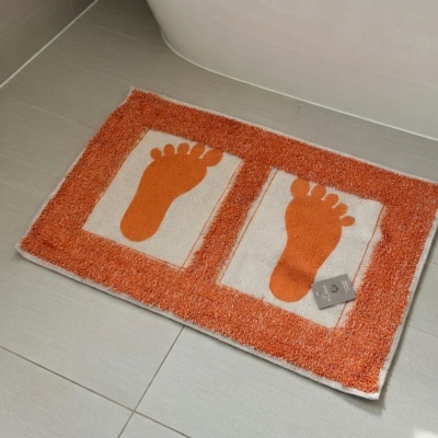 Tapete de banheiro branco e laranja com pegadas laranjas sobre chão de azulejos cinza