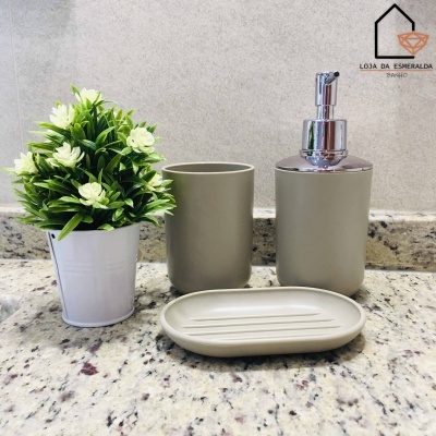 Conjunto de acessórios de casa de banho cinzentos junto a planta artificial em vaso branco