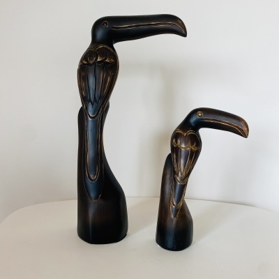 Esculturas de madeira de pássaros em tons escuros com detalhes dourados, sobre superfície branca.