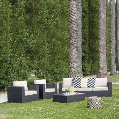 Conjunto de mobiliário de exterior em rattan sintético preto com almofadas claras e decorativas em relva com palmeiras.