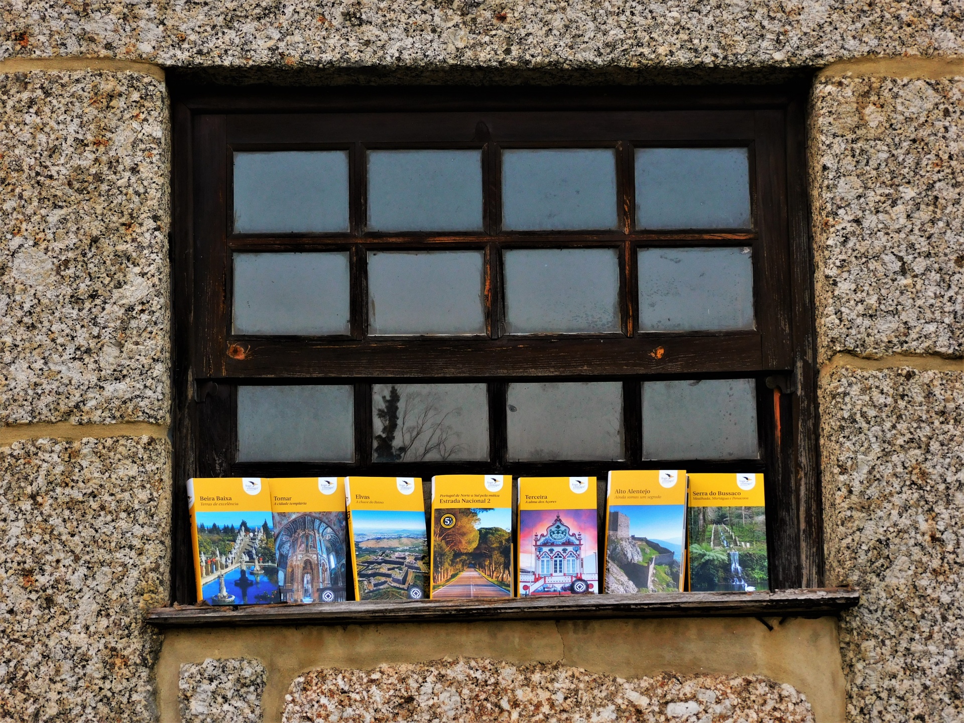 Janela de madeira preta com postais coloridos no peitoril numa parede de pedra