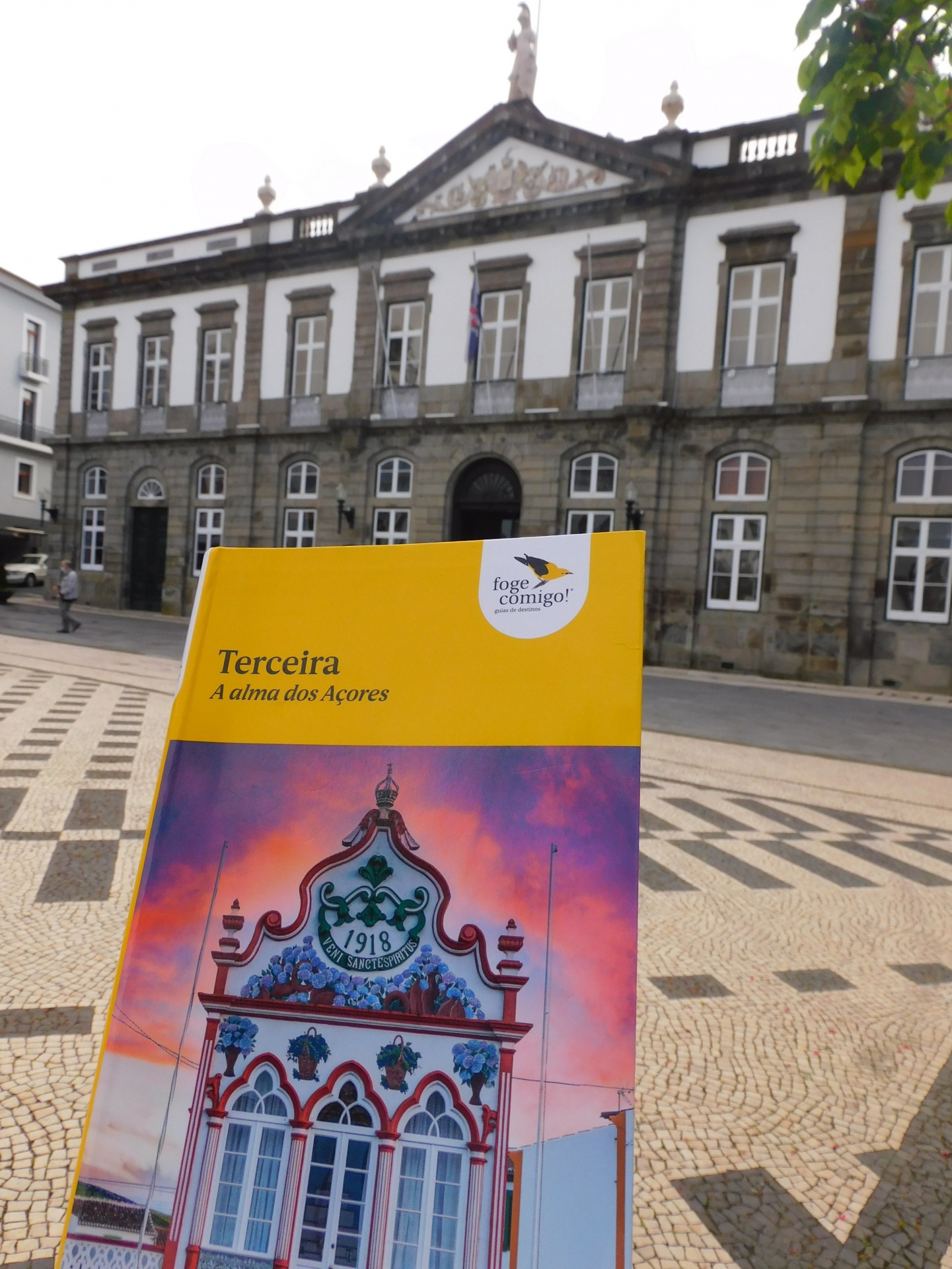 Livro de capa amarela sobre a Terceira e um edifício clássico cinzento ao fundo