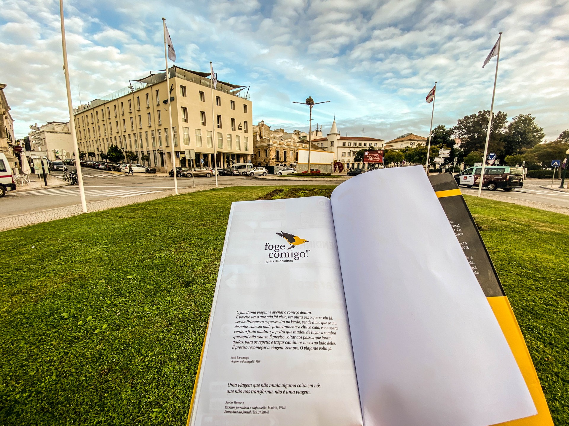 Livro aberto na relva com edifícios ao fundo e céu nublado