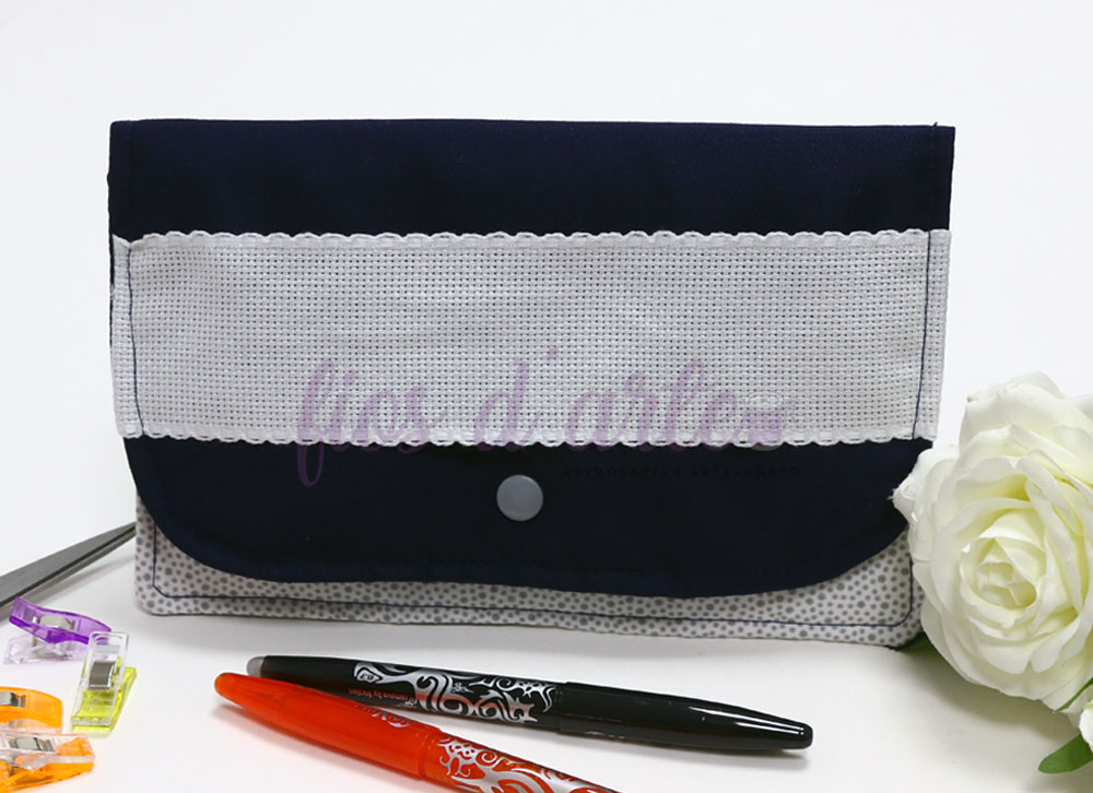 Bolsa de tecido azul escuro com faixa branca translúcida e botão de pressão, canetas, ganchos e flor