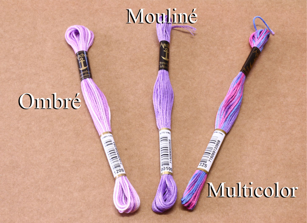 Três novelos de fio para bordar em tons de púrpura e rosa com etiquetas distintas