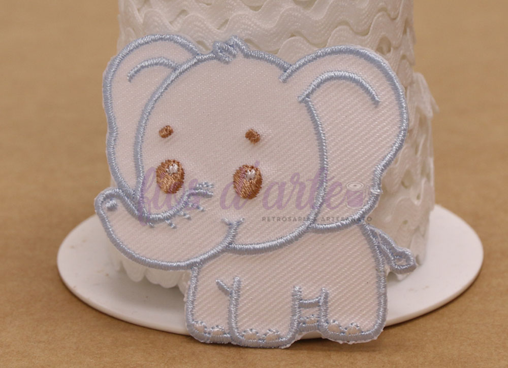 Aplicação termocolante Elefante (5x5,2cms) - azul Bordado de elefante cor de creme com contornos cinzentos em frente a um rolo de fita branca