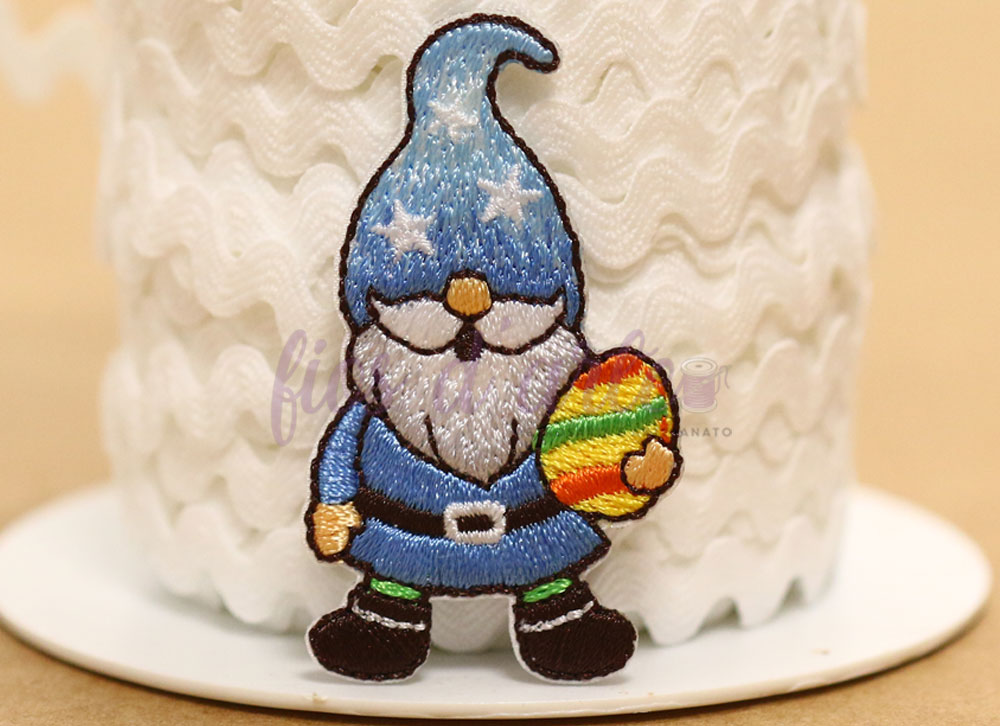 Aplicação termocolante Gnomo Ovo da Páscoa (4,5x2,5cms) Patch bordado de gnomo azul segurando ovo colorido colocado em rolo de fita branca