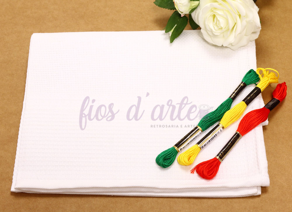 Toalha branca com novelos de linha colorida e rosa branca sobre fundo castanho