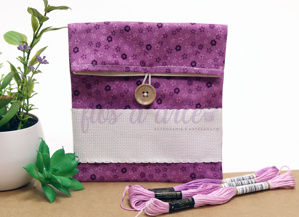 Bolsa Multiusos estampada com quadrilé para bordar ponto cruz (14x15cms) - florzinhas lilás Bolsa rosa com padrão de flores e botão de madeira, plantas em vasos e novelos de linha rosa