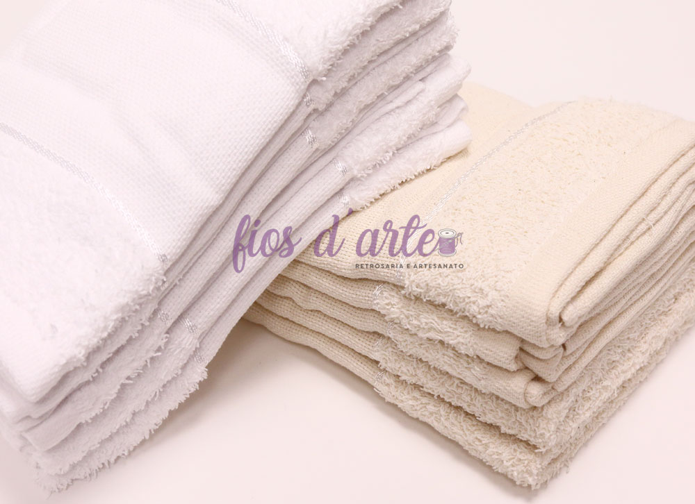 Duas pilhas de toalhas de banho dobradas, branca e bege, em fundo branco