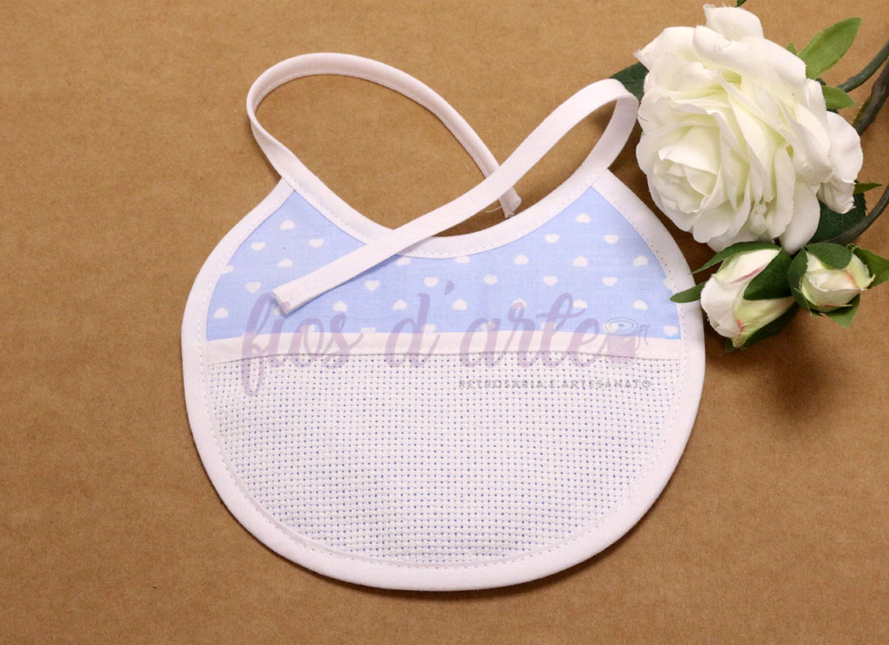 Babete redondo em tecido azul com padrão de nuvens brancas e tecido branco para bordado