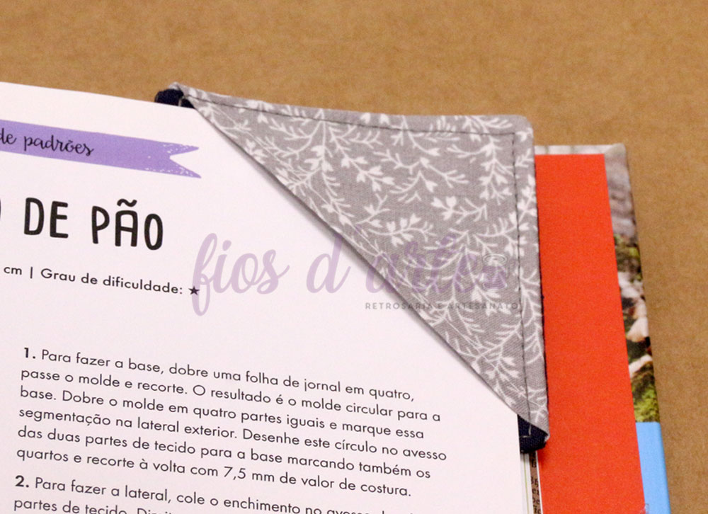 tecido cinza padrão floral colocado sobre página de livro com texto em português