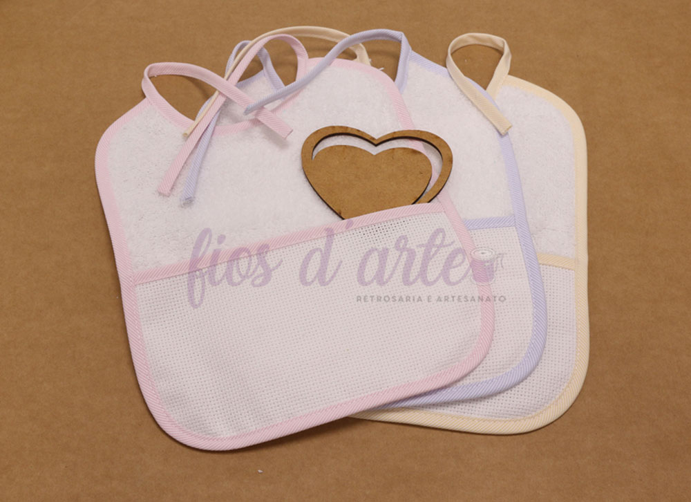 Três babetes de bebé brancos com bordas coloridas e um coração de madeira