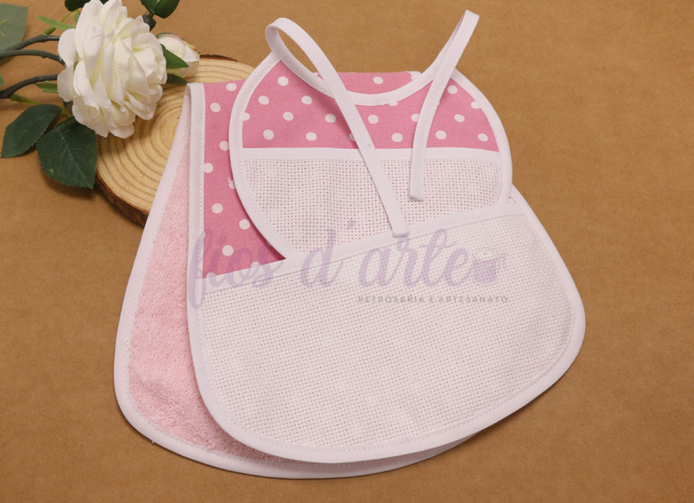 Babete rosa com bolinhas brancas e babete rosa claro com parte frontal em malha e fita para amarrar, ambos sobre superfície castanha