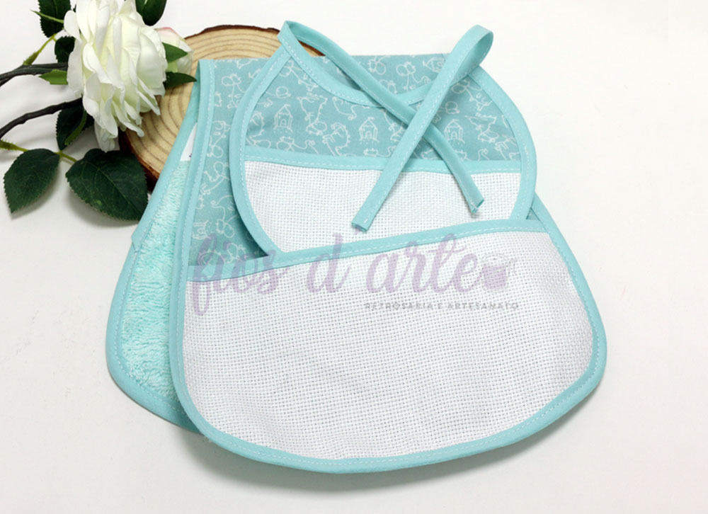 Babetes de bebé azuis com diferentes texturas e padrão infantil, junto a uma flor branca.