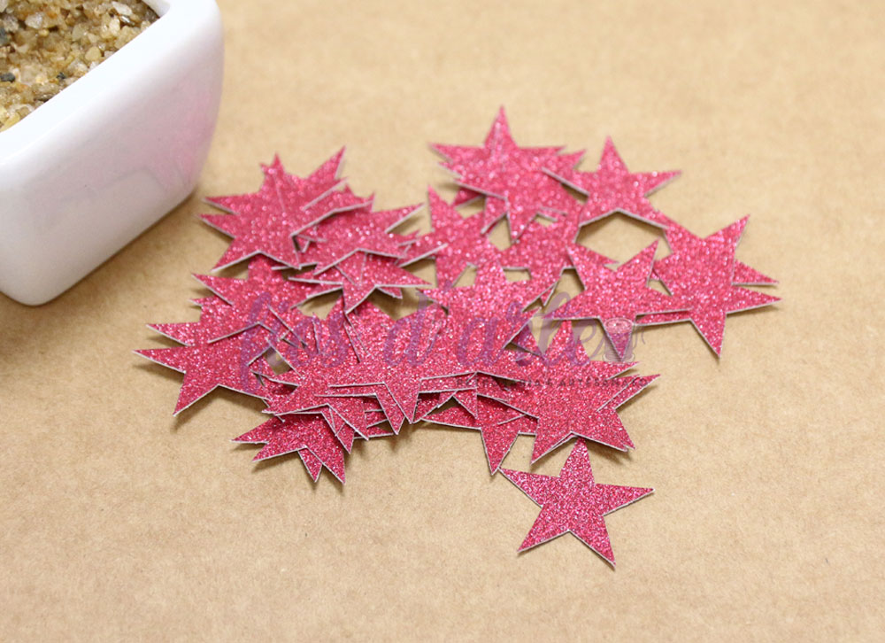 Estrelas decorativas cor-de-rosa com brilho sobre superfície castanha perto de vaso branco.