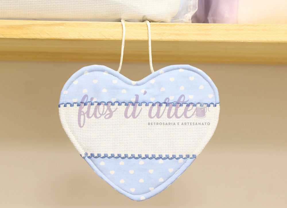 Almofada em forma de coração azul claro com bolinhas brancas pendurada numa prateleira de madeira