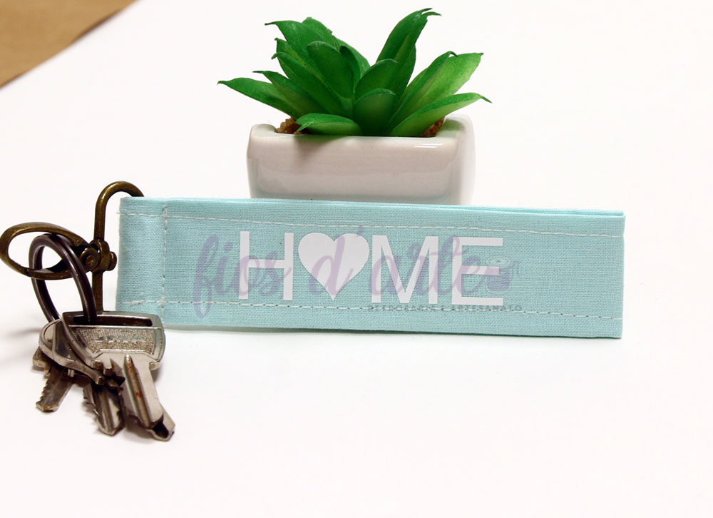 Chaveiro tecido azul claro com texto HOME e coração, chaves e planta artificial