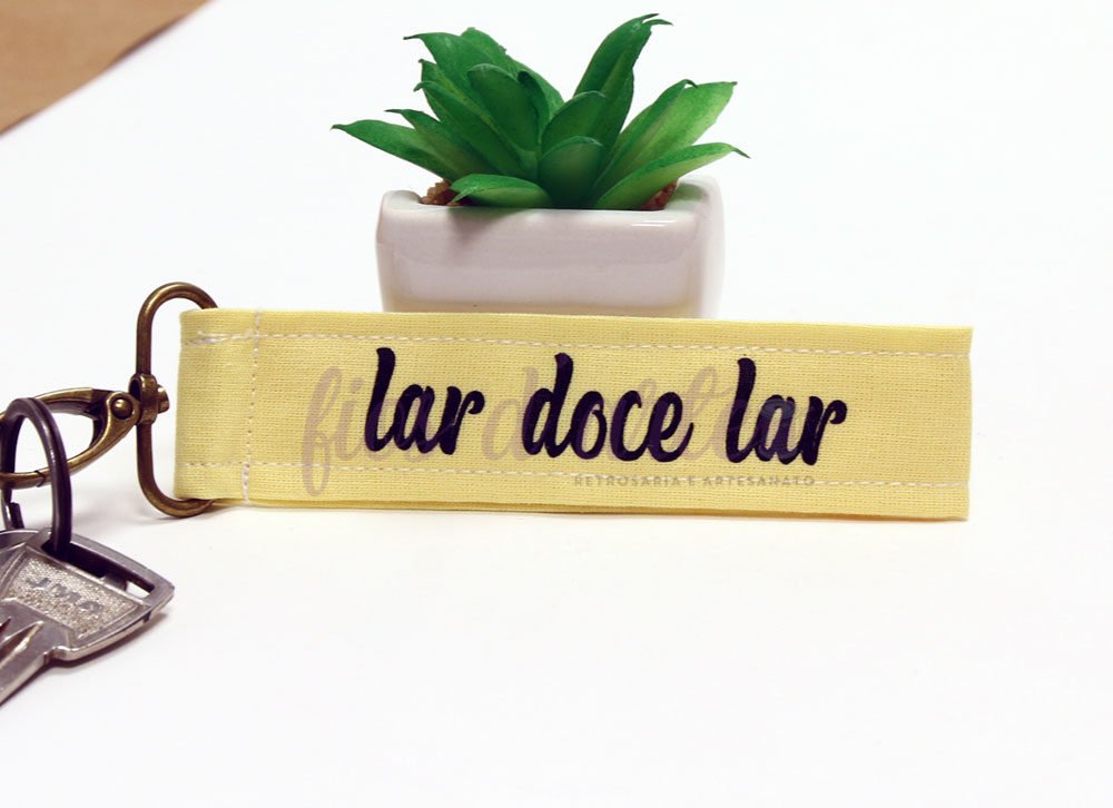 Chaveiro amarelo com texto 'lar doce lar' e planta suculenta em vaso branco