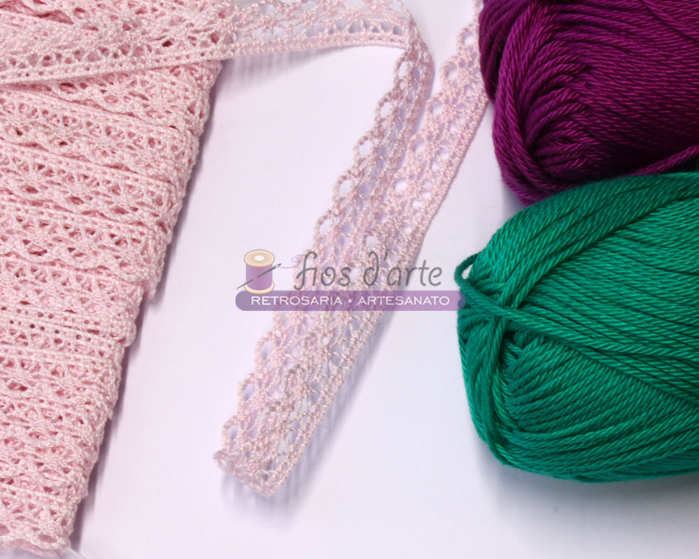 Renda com bico (10mm) - rosa bebé Tecido de renda rosa, meadas de lã verde e roxa, fita rendada rosa sobre superfície branca com logótipo Fios e Arte