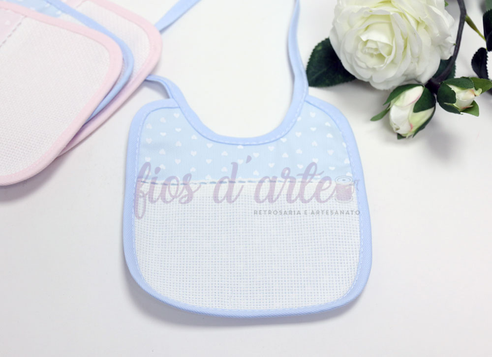 Babete para bebé azul com corações brancos e borda azul junto a rosas brancas.