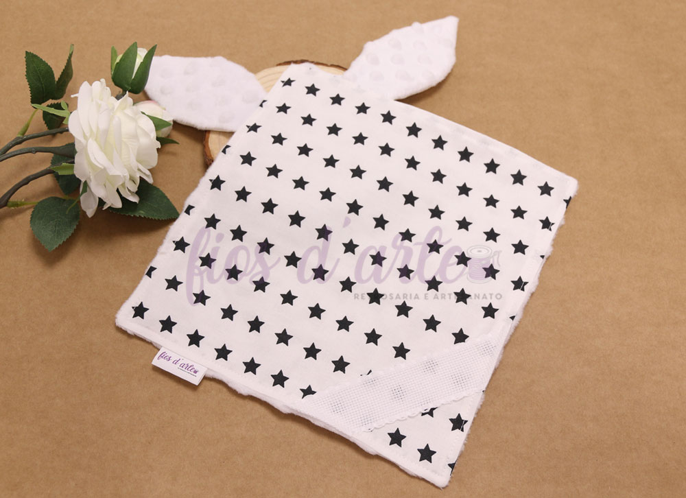 Doudou/ Naninha Orelhinhas com minky para bordar ponto cruz #08 (Fios d'arte) Toalha de rosto branca com estrelas pretas e orelhas pontudas sobre superfície castanha ao lado de flor branca