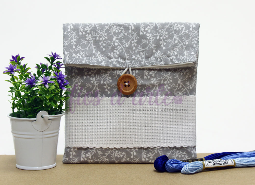 Bolsa de tecido cinzento com padrão floral, botão de madeira, planta em vaso branco e novelos de linha azul