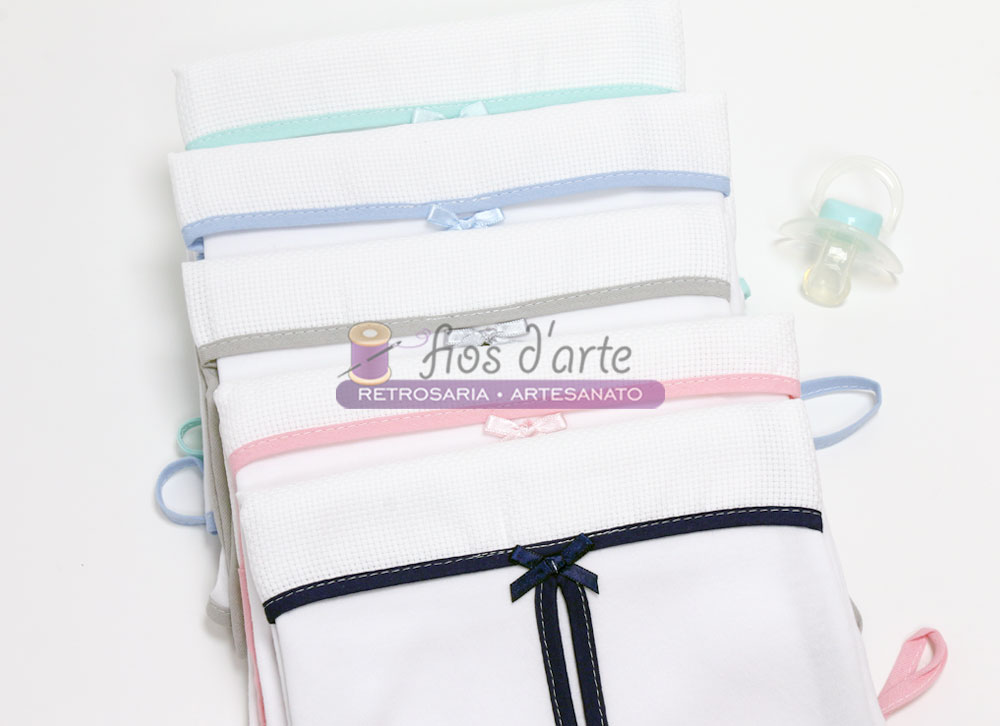 Conjunto de fraldas brancas com bordas coloridas e laços, e chupeta ao lado