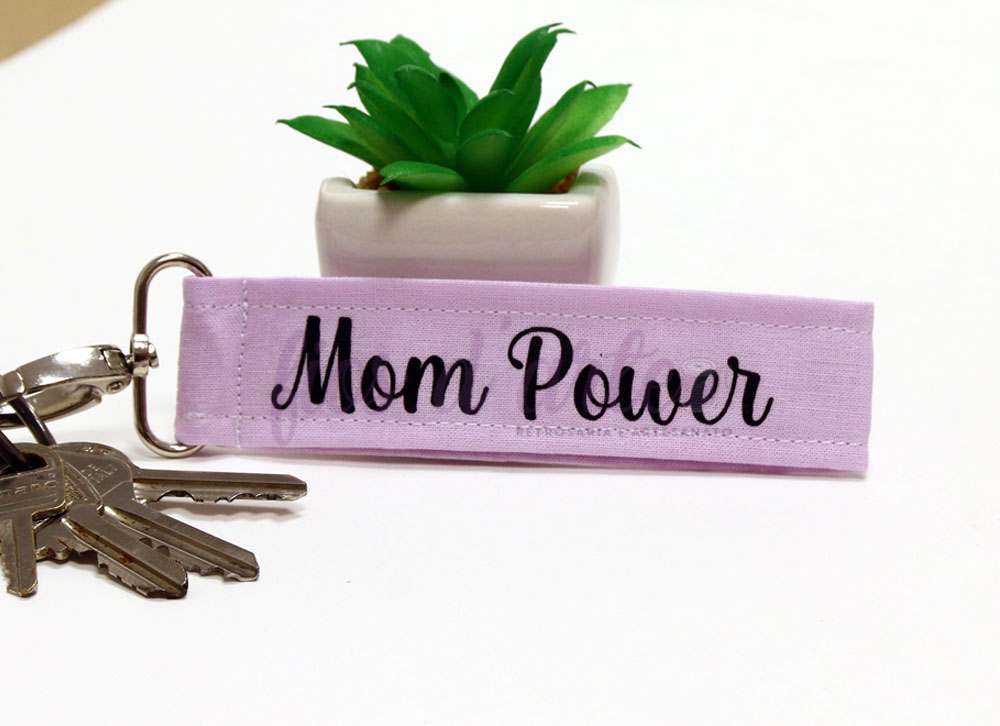 Chaveiro lilás com texto Mom Power, conjunto de chaves e planta artificial