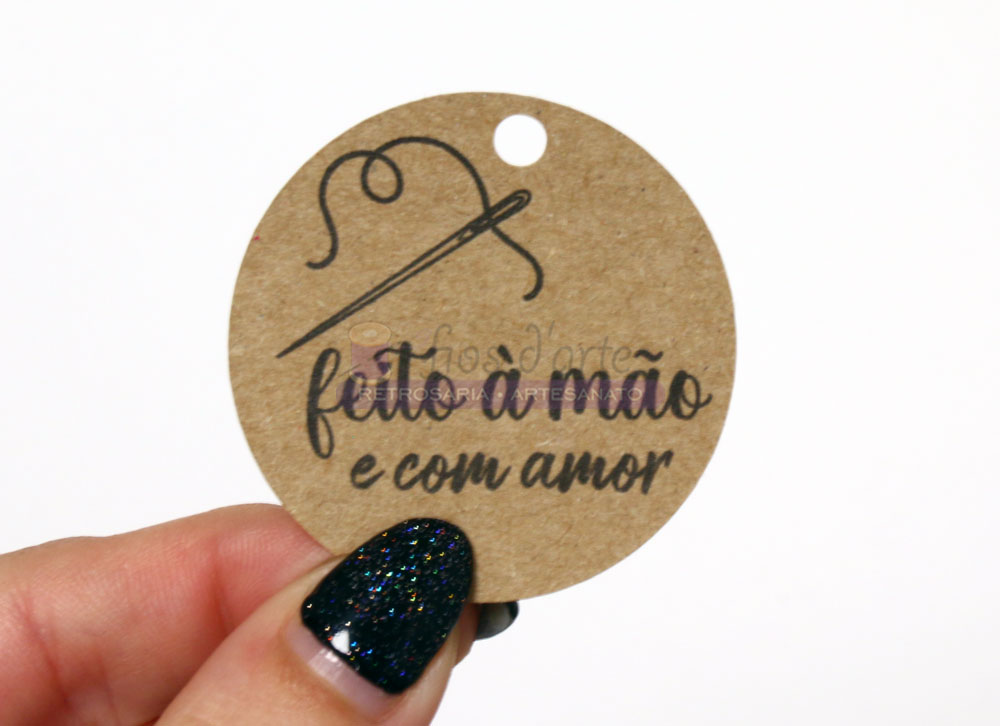 Etiqueta redonda de papel com texto feito à mão e com amor, segurada por uma mão com unhas pintadas de preto com brilhos