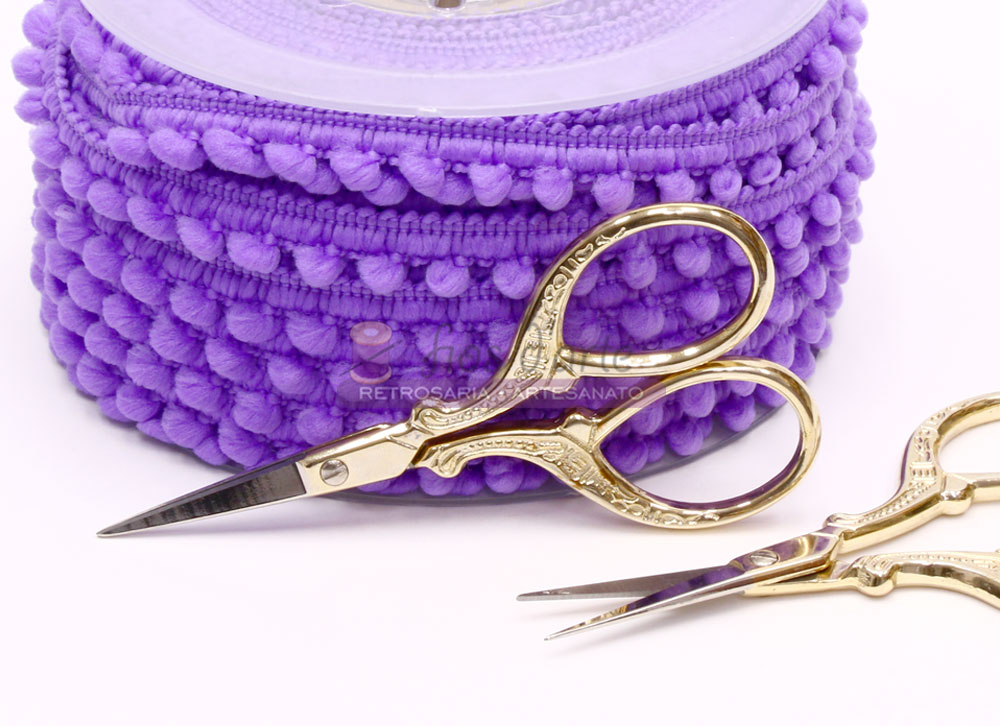 Tesouras douradas ornamentais com fita de pompons roxa ao fundo